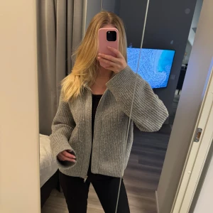 Grå ribbad kofta med dragkedja - Säljer en stilren grå kofta med ribbad struktur och dragkedja framtill. Koftan har långa ärmar och en bekväm passform, perfekt för kyligare dagar. Ett mångsidigt plagg som passar till det mesta i garderoben.