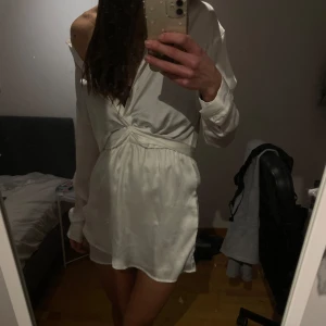 Vit omlottklänning -  vit omlottklänning med lång ärm och knytning i midjan. Klänningen har knappar framtid så man kan göra sin egna passade v-ringade design och är tillverkad i ett glansigt material. Perfekt för speciella tillfällen som studenten❣️