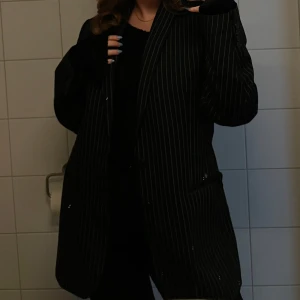 Svart randig kavaj från Batistini - Snygg svart kavaj med vita ränder. Kavajen har två knappar framtill och klassiska fickor. Perfekt för en stilren look.