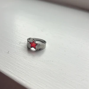 Silverring med röd stjärna - Snygg silverring med en röd stjärna i mitten. Perfekt för att ge en färgklick till din outfit. Ringen har en enkel och stilren design som passar till många olika stilar.