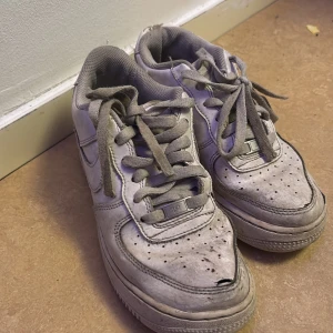 Grå Nike Air Force sneakers - Säljer ett par grå Nike Air Force sneakers med klassisk design och snörning. Skorna har en robust sula och är tillverkade i syntetmaterial. Perfekta för en avslappnad stil. (Pris kan diskuteras)