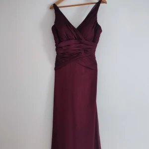 Vinröd lång/balklänning  - Elegant vinröd långklänning med djup v-ringning och draperad design. 