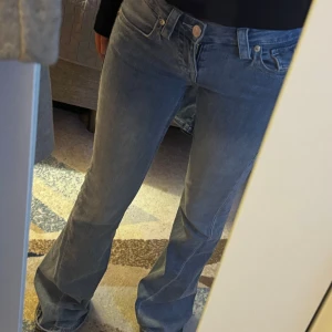 Blå bootcut jeans från Wrangler - Säljer ett par snygga blå bootcut jeans från True religion. De är i bra skick och har en klassisk femficksdesign med knappar och dragkedja. Perfekta för både vardag och fest! Jag är 167cm lång!