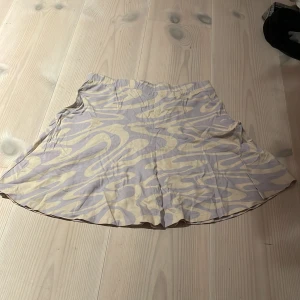 Mönstrad kjol från H&M - Säljer en superfin kjol från H&M i storlek 164. Den har ett coolt abstrakt mönster i lila och beige. Kjolen är kort och perfekt för sommardagar. Materialet känns lätt och bekvämt, vilket gör den idealisk för både vardag och fest. Passa på att uppdatera garderoben med denna snygga kjol!