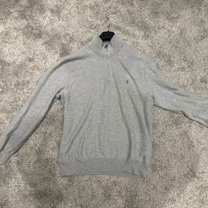 Ralph Lauren halfzip  - Säljer en stilren grå tröja från Polo Ralph Lauren i storlek L. Tröjan har en dragkedja vid halsen och är perfekt för både vardag och lite finare tillfällen. Den är i mycket bra skick och passar perfekt till höst och vår.