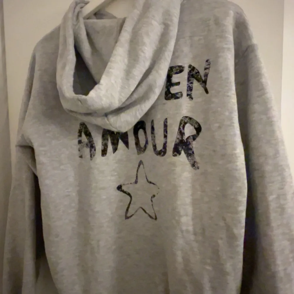 Säljer en mysig grå hoodie med texten 'JE M'EN AMOUR'. Perfekt för en avslappnad stil och kyliga dagar. Den har en klassisk passform med långa ärmar och en bekväm huva. Perfekt för både vardag och mysiga hemmakvällar. Är i storlek 170, men sitter som S. . Hoodies.