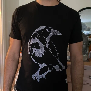 Svart t-shirt med fågeltryck - Säljer en svart t-shirt med ett coolt fågeltryck i vitt. Den är kortärmad och har en normal passform. Perfekt för vardagsbruk eller en avslappnad dag ute.