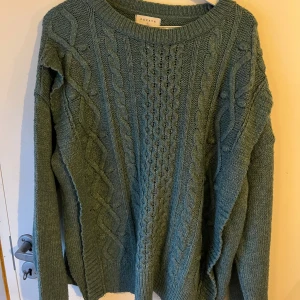 Grön stickad tröja från Papaya - Mysig grön stickad tröja från Papaya i storlek L. Tröjan har ett snyggt flätmönster på framsidan och är tillverkad av 75% akryl och 25% polyester. Perfekt för kyliga höst- och vinterdagar.