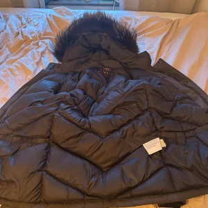 Dunjacka herr woolrich - Säljer en svart dunjacka från Woolrich i mycket bra skick. Jackan har en mysig pälskantad huva och stora fickor med knappar framtill. Perfekt för kalla vinterdagar! 🖤pris kan diskuteras.