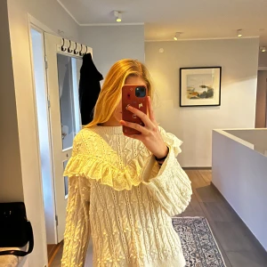 Vit stickad tröja med volangdetaljer - Superfin vit stickad tröja med volangdetaljer på axlarna. Perfekt för höst och vinter, den är både mysig och stilren. Tröjan har långa ärmar och ett klassiskt mönster som ger en extra touch. Passar perfekt till både jeans och kjol!