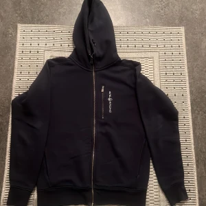 Svart hoodie från Sail Racing - Säljer en navy blåhoodie från Sail Racing i storlek S. Den har en dragkedja framtill och en mysig huva. Perfekt för kyliga dagar och har en stilren design med logga på bröstet. Passar både till vardags och för avslappnade aktiviteter.