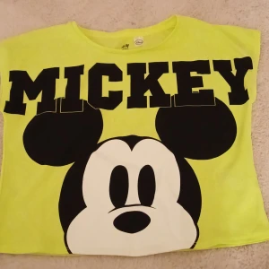 Gul t-shirt med Mickey Mouse från H&M - Säljer en cool gul t-shirt från H&M med stort tryck av Mickey Mouse i svart.  Träningsmaterial