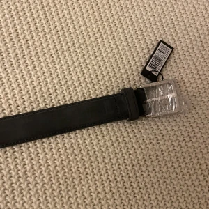 Svart skinnbälte från Dissing - Säljer ett snyggt svart skinnbälte från Dissing i nytt skick. Bältet har en stilren design med en silverfärgad spänne som fortfarande är inplastad. Perfekt för både vardag och fest! 🖤