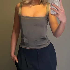 Gråbrun korsettopp  - Tvärsnygg grå korsettopp i satinmaterial med breda axelband och dragkedja i ryggen. Går att styla både upp och ner! Toppen sitter tight och framhäver både midja och byst superfint⭐️Köpt på Zara för ett tag sen men är totalt oanvänd! Hör av dig vid frågor⭐️