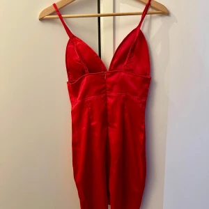 Röd axelbandslös klänning - Snygg röd klänning i satin med smala axelband och en figurnära passform. Perfekt för festliga tillfällen! Klänningen har en dragkedja i ryggen för enkel påklädning.