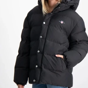 Svart dunjacka med huva - Sparsamt använd, nypris är 2300kr! Säljer en svart dunjacka med huva, perfekt för kalla dagar. Jackan har en dragkedja och knappar framtill för extra skydd mot kylan. Den är långärmad och har en normal passform. Supermysig och varm