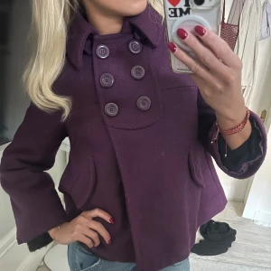 Kort kappa med knappar - Säljer en snygg lila kappa med dubbelknäppning och stor krage. Perfekt för höst och vår när du vill vara både stilren och varm. 