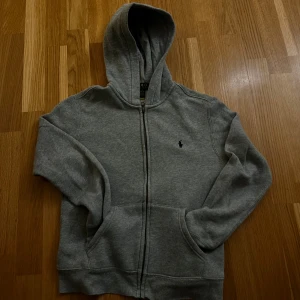 Grå hoodie från Ralph Lauren - Säljer en klassisk grå hoodie från Ralph Lauren i storlek m(10-12).väldigt bra skick för jag bara kunde använda den i 2 månader för jag väckte ut ur den