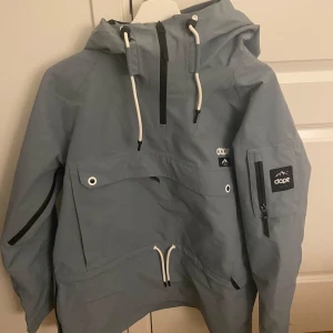 Dope jacka grå - Säljer en grå/ lite blå aktig jacka från Dope i storlek L. Jackan har en praktisk huva, dragkedjor, fickor och snören. Skyddar mot kyla, vind och regn.                                            Den är i mycket bra skick, bara använts 2 gånger till skidåkning. Original pris är 1900kr