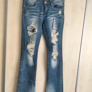 Blå slitna jeans från Machine - Säljer ett par coola blå jeans från Machine med slitna detaljer på framsidan och bakfickorna. Det är storlek 5 alltså typ S. De är low waist och Flare.