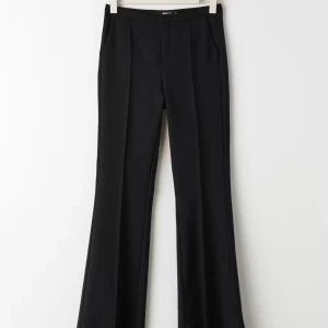 Svarta kostymbyxor - Snygga svarta kostymbyxor i högmidjad modell. De har en elegant bootcut-stil som ger en fin siluett. Perfekta för både kontoret och festliga tillfällen. Materialet känns mjukt och bekvämt, vilket gör dem sköna att bära hela dagen.