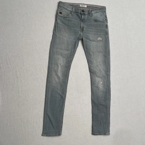 Grå jeansbyxor från Blend - Säljer ett par grå jeans från Blend i bra skick. De har en snygg sliten look med ljusa partier och en liten reva på framsidan. Klassisk femficksdesign med knapp och dragkedja. Perfekta för en avslappnad stil! Slim fit. Strl w31l34