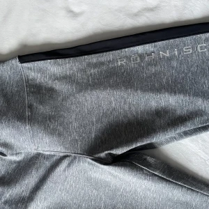 Grå träningsbyxor från Röhnisch - Säljer ett par grå träningsbyxor från Röhnisch. De är i ett mjukt och stretchigt material, perfekt för träning. Byxorna har en svart detalj längs sidan och en bekväm passform. Perfekta för gymmet eller en löprunda!