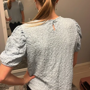 Ljusblå topp från Zara - Säljer en superfin ljusblå topp från Zara i storlek 13-14 år. Toppen har korta puffärmar och ett snyggt spetsmönster vid ärmarna och nederkanten. Den har en liten knäppning i nacken och är perfekt för både vardag och fest. 🩵