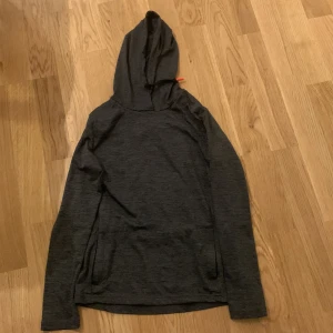 Mörkgrå hoodie - Säljer en mörkgrå hoodie i mycket bra skick. Den är tillverkad av 85% polyester och 15% elastan, vilket gör den både bekväm och stretchig. Perfekt för höst och vinter med sin långa ärmar och mysiga huva. Passar bra för träning eller en avslappnad dag hemma.