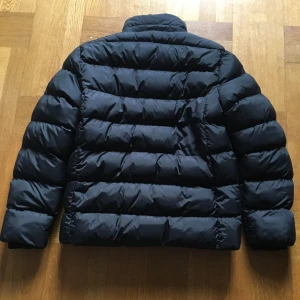 Svart pufferjacka från Vinson - Säljer en svart pufferjacka från Vinson i mycket bra skick. Jackan har en cool broderad detalj med nummer 23 och texten 'Vinson Original' på bröstet. Den är perfekt för kalla dagar med sin tjocka vaddering och dragkedja framtill. Passar perfekt för vintern! ❄️