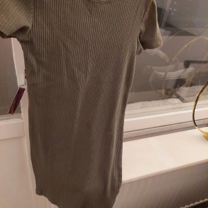 Olivgrön ribbad klänning från XOXO Friends - Säljer en superfin olivgrön ribbad klänning från XOXO Friends. Den har en enkel och stilren design med korta ärmar och en bekväm passform. Perfekt för både vardag och lite finare tillfällen. Passar bra till höst och vår!