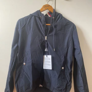 Mörkblå vindjacka från Moncler - Säljer en snygg mörkblå vindjacka från Moncler. Jackan har en dragkedja framtill och justerbar huva med dragsko. Perfekt för vår och höst! Den är i mycket bra skick och har Monclers logga på ärmen. Passar perfekt för en casual look.