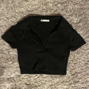 Svart ribbad topp från Zara - Säljer en svart ribbad topp från Zara i storlek S. Toppen har en djup v-ringning och korta ärmar, perfekt för både vardag och fest. Den är i bra skick och passar till många olika outfits. 🖤