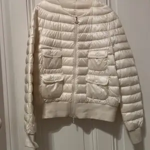 Säljer en snygg benvit dunjacka från Moncler i nyskick. Jackan har en quiltad design med dragkedja och två praktiska fickor framtill. Perfekt för kyliga höst- och vinterdagar. Den är både stilren och varm, vilket gör den till ett måste i garderoben!