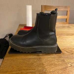 Svarta boots från H&M storlek 34 - Säljer ett par svarta boots i skinn från H&M. De har en robust sula och dragkedja på sidan för enkel på- och avtagning. Perfekta för höst och vinter med sin stilrena design och bekväma passform. Använda men i  riktigt bra skick.