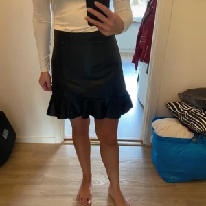 Skinnimitation kjol - Kjol i skinnimitation från hm. Storlek 38(divided). Med volang och dragkedja baktill.