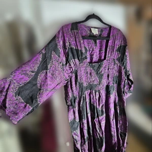 Lila och svart blus/klänning från Masai - Säljer en unik lila och svart blus/klänning från Masai i storlek XL. Den har ett abstrakt mönster och är tillverkad i ett skönt material som ger en loose passform. Perfekt för höst och vår med sina trekvartsärmar och v-ringade hals. Inga defekter, endast lite skrynklig vid fototillfället.