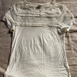 Vit spetsdetaljerad topp från H&M - Säljer en söt vit topp från H&M i storlek S. Den har korta ärmar och vackra spetsdetaljer över bröstet som ger en fin touch. Perfekt för vår och sommar! 🌺 