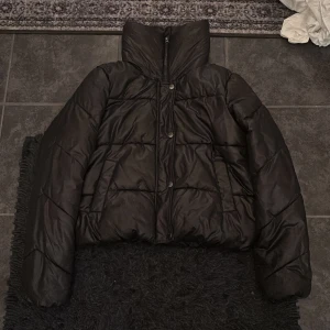 Svart pufferjacka - Säljer en svart pufferjacka i mycket bra skick. Den har en hög krage och stängs med både dragkedja och knappar. Nyskick, storlek XS