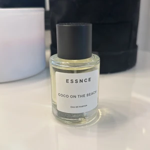 Coco on the Beach Eau de Parfum från Essnce - Säljer en fräsch och somrig Eau de Parfum från Essnce med namnet 'Coco on the Beach'. Flaskan är stilren och genomskinlig med en enkel vit etikett och svart kork. Perfekt för att fånga känslan av en dag vid stranden! Som man ser är den endast använd några gånger.