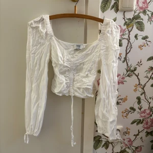 Blus NA-KD - En vit blus från nakd. Med snöre mitt på så man kan reglera längden. Strl 34. Använd 2 ggr för 3/4 år sedan och sen har den fått ligga i garderoben. 