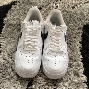 Vita Nike Air Force sneakers - Säljer ett par klassiska vita Nike Air Force sneakers. De har en stilren design med svart Nike-logga på sidan och är i nyskick. Perfekta för både vardag och fest!