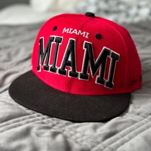 Röd och svart keps från Raw Blue - Säljer en snygg keps i mycket fint skick . Kepsen har texten 'MIAMI' broderad både fram och bak. Den har en justerbar passform. 