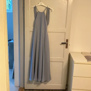 Ljusblå långklänning - Säljer en elegant ljusblå långklänning med smala axelband och en vacker öppen rygg. Perfekt för sommarens fester eller en bal. Klänningen har en flytande passform som ger en drömlik känsla. Priset kan diskuteras