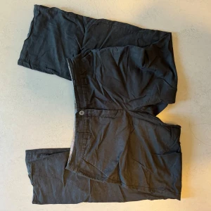 Svarta byxor från Yessica - Säljer ett par svarta linnebyxor från Yessica. De har en klassisk design med knappar bak och en bekväm passform. Storlekslappen är bortklippt men de passar M/L