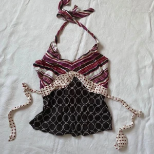Flerfärgad y2k halterneck topp - Unik 2000tals halterneck topp med ett färgglatt randigt mönster i rosa, lila och vitt upptill och röda polkadots, mörkbrun nedtill. Toppen har knytband i midjan med prickigt mönster. Perfekt för en somrig look!