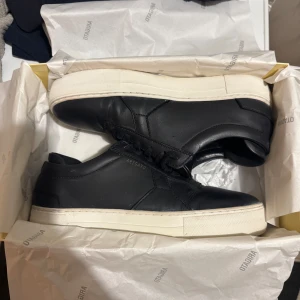 Svarta sneakers från Axel Arigato - Snygga svarta sneakers från Axel Arigato med vit sula och diskret snörning. Tillverkade i skinn för en stilren look. Perfekta för en minimalistisk stil. Köpta för 2250kr
