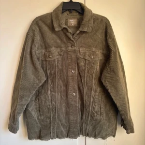 Olivgrön manchesterjacka - Säljer en olivgrön manchesterjacka med knappar framtill och två bröstfickor. Jackan har en avslappnad passform och långa ärmar. 