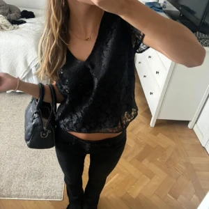 Svart spetsblus - Säljer en elegant svart spetsblus med v-ringning och korta ärmar. Perfekt för en stilren look. Blusen har ett vackert genombrutet mönster som ger en sofistikerad touch.