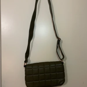 Olivgrön  axelväska - Snygg olivgrön axelväska med quiltat mönster. Väskan har en justerbar axelrem och stängs med en tryckknapp. Oanvänd